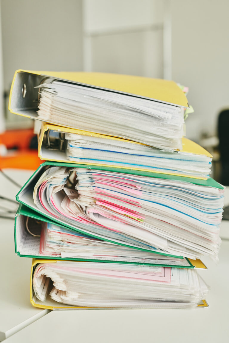 Primer plano de la mesa con una pila de carpetas coloridas llenas de archivos muertos con notas adhesivas adjuntas en una oficina